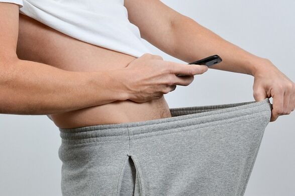 a man looks down his pants at an enlarged penis